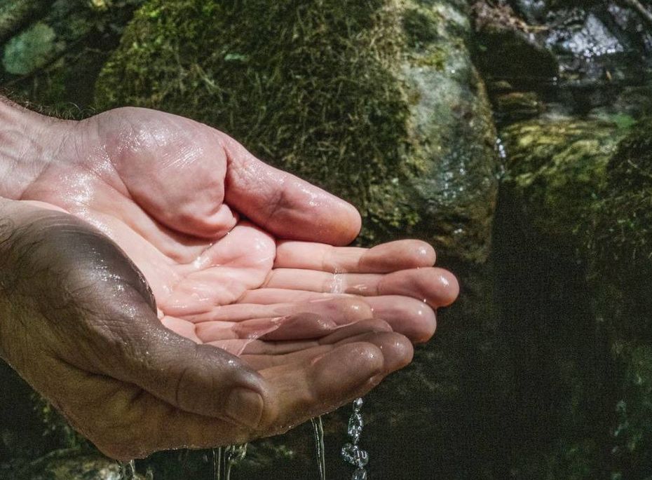 Hände unter Wasser im Wellnessbereich Eine Hand hält Wasser unter einem kleinen Quelllauf zwischen moosigen Steinen.