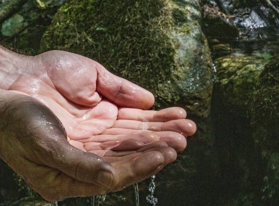 Hände unter Wasser im Wellnessbereich Eine Hand hält Wasser unter einem kleinen Quelllauf zwischen moosigen Steinen.