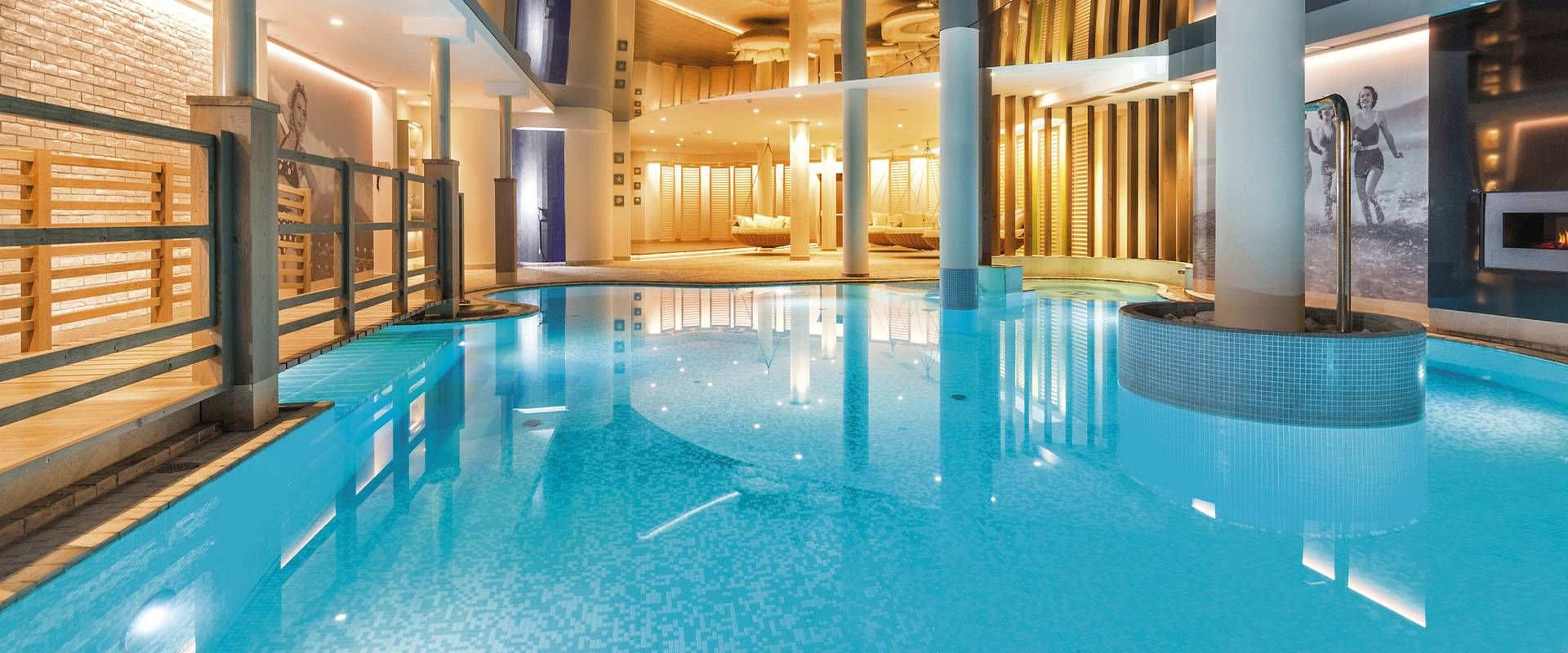 Ein heller Innenpool mit Thermalwasser im Spa, umgeben von Holz, Glas und warm beleuchteten Ruhebereichen.