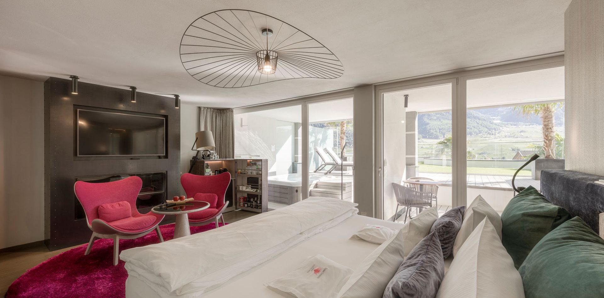 Ein großes Bett und ein Sitzbereich mit pinken Sesseln in einer hellen Luxussuite mit Blick auf den Balkon.
