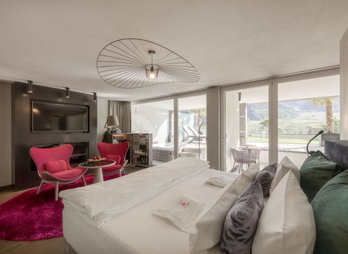 Ein großes Bett und ein Sitzbereich mit pinken Sesseln in einer hellen Luxussuite mit Blick auf den Balkon.