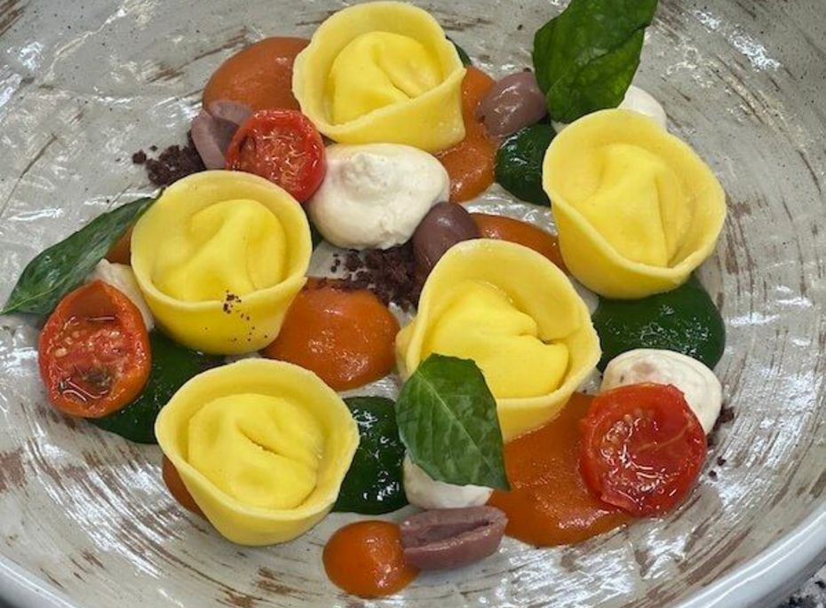 Tortellini mit Tomaten und Basilikum im Preidlhof Eine Schüssel mit gelben Tortellini, Kirschtomaten, Basilikumblättern und kleinen Soßenakzenten.