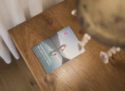 Una brochure è appoggiata su un tavolo in legno accanto alle tende, con un elemento sfocato in primo piano.
