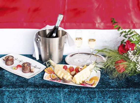 Champagner im Eiskübel, zwei gefüllte Gläser und ein Teller mit Früchten und Desserts auf einem Tisch.