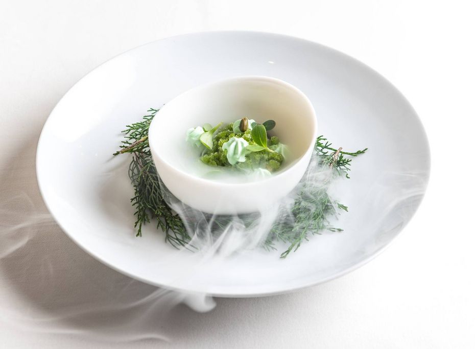 Gourmetvorspeise im Preidlhof in Naturns Eine weiße Gourmetvorspeise in einer Schale liegt auf einem Teller, umgeben von Kräutern und feinem Dampf.