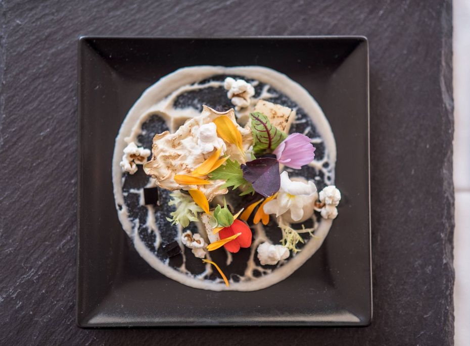 Dessertteller im Gourmetrestaurant im Preidlhof Ein kunstvoll angerichteter Dessertteller auf einem schwarzen Teller mit essbaren Blüten und feinen Garnituren.