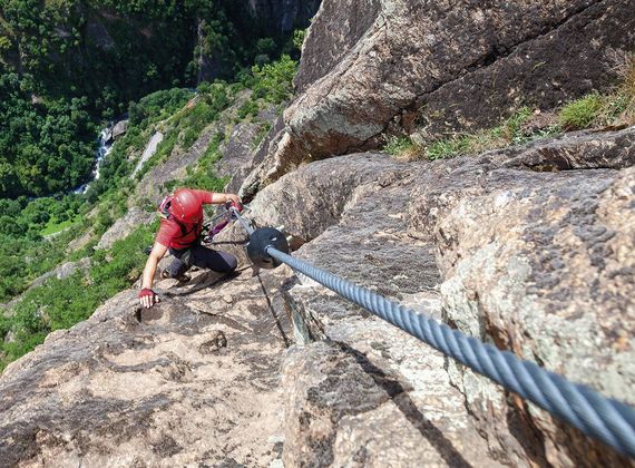 Ein Kletterer steigt an einer steilen Felswand mit gesichertem Seil im Vinschgau auf.