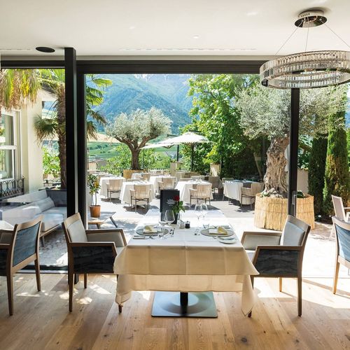 Ein helles Gourmetrestaurant mit gedeckten Tischen und großer Glasfront zum Garten und zu den Bergen.