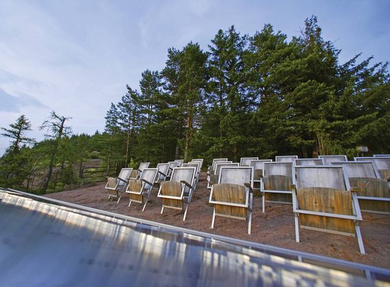 Mehrere Ruheliegen stehen am Beckenrand vor einem bewaldeten Hang.
