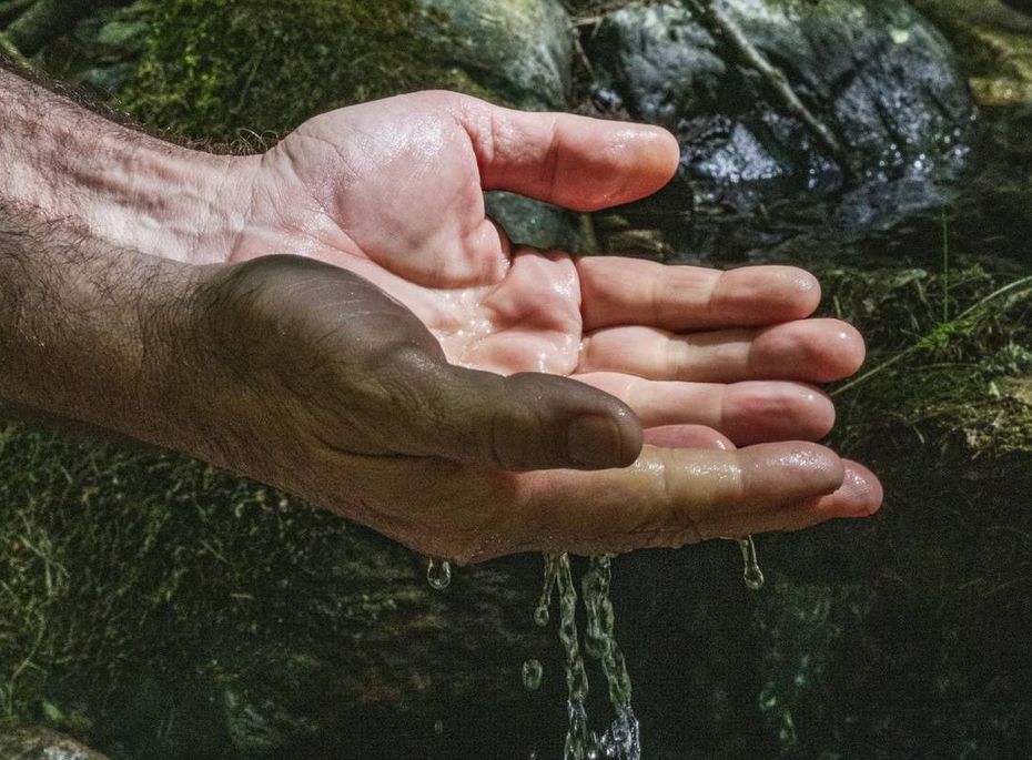 Hände unter einem Wasserlauf im Wellnessbereich Zwei Hände halten sich unter einem kleinen Wasserlauf zwischen moosigen Steinen im naturnahen Wellnessbereich.