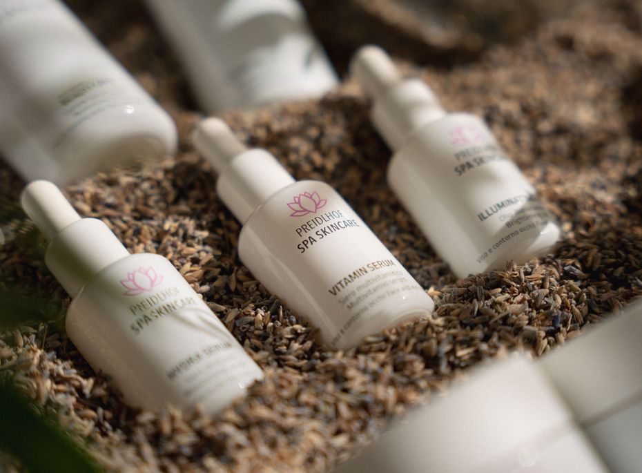 Preidlhof Spa Skincare Produkte im Arrangement Mehrere weiße Spa-Skincare-Fläschchen liegen in einem dekorativen Naturbett aus Steinen und Pflanzenmaterial.