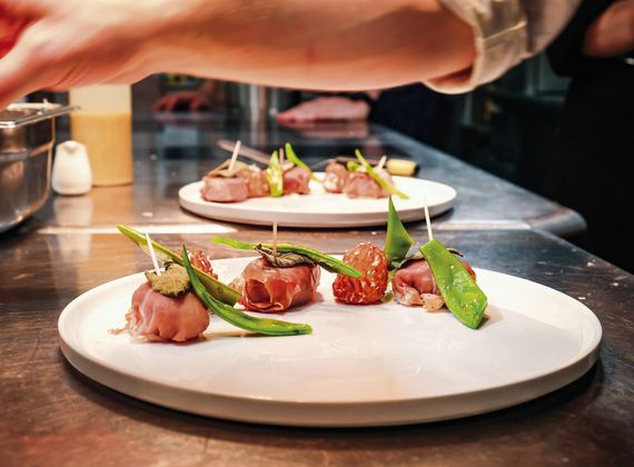 A chef plates small gourmet appetizers on white plates in a restaurant kitchen.