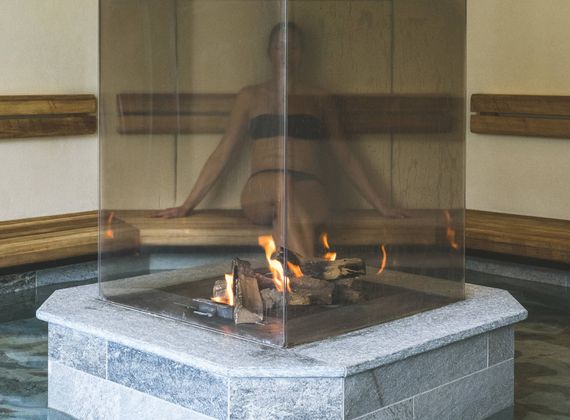 A person sits behind a glass fire feature in the sauna relaxation area.