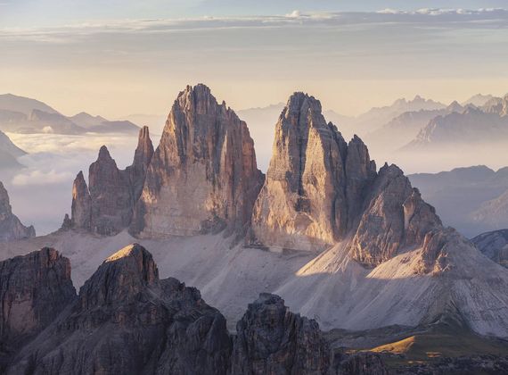 Die Dolomiten mit markanten Felsgipfeln liegen im warmen Morgenlicht und über einem stillen, hellen Talkessel.