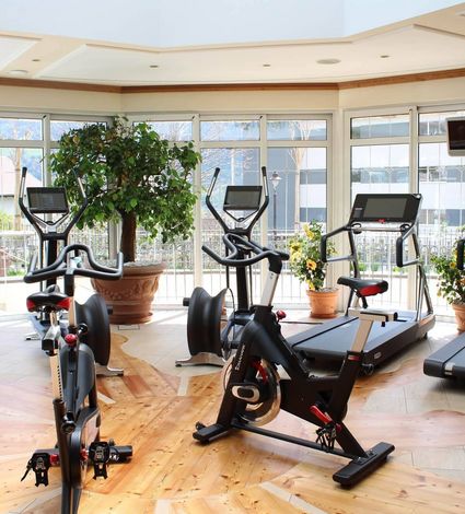 Ein heller Fitnessraum mit Laufbändern, Ergometern und weiteren Cardiogeräten vor großen Fenstern.
