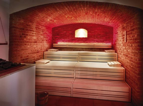Eine Sauna mit Holzliegen und roter Backsteinwand unter einer gewölbten Decke.