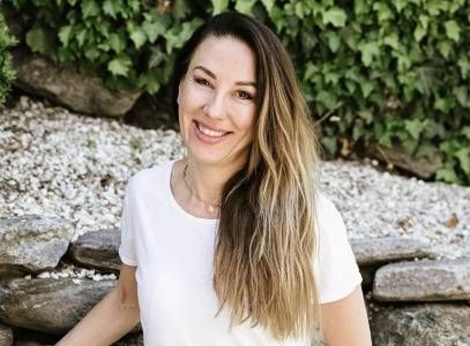 Porträt einer Frau vor Steinmauer im Garten Eine Frau mit langem Haar lächelt vor einer Steinmauer und grünem Blätterhintergrund im Garten.