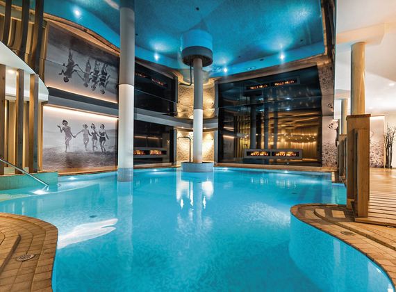 Ein heller Innenpool im Spa mit Holzliegen, Glaswänden und warmem Licht im Preidlhof.