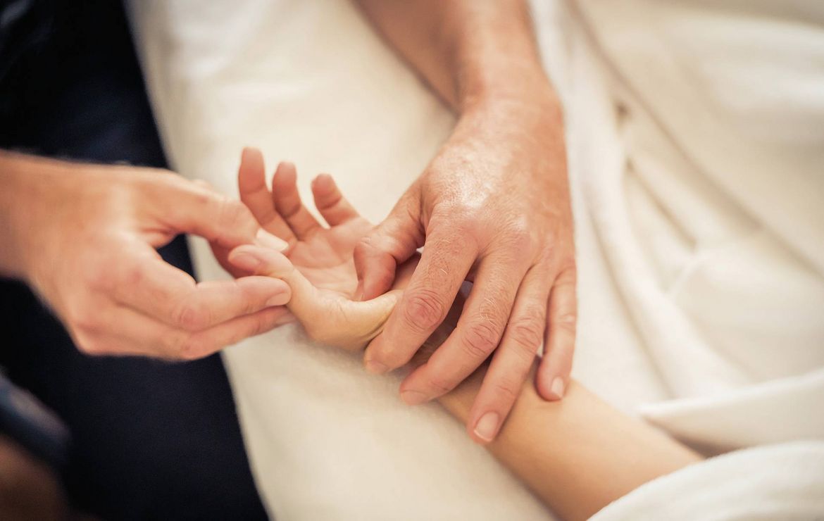 Eine Hand wird bei einer Massage sanft an den Fingern und dem Handgelenk gehalten.