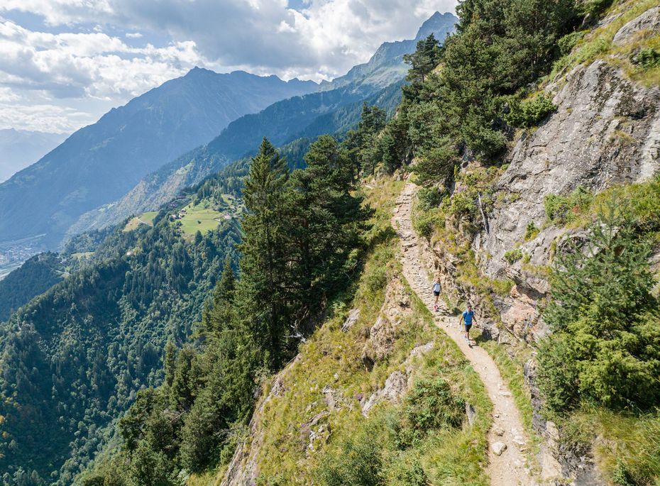 Wanderweg am Berghang in Südtirol Zwei Wanderer gehen auf einem schmalen Pfad entlang eines steilen Berghangs mit Blick ins Tal.