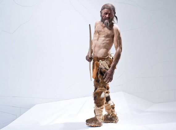 Un'esposizione a grandezza naturale di un uomo dell'età della pietra è in piedi su una pedana bianca, con un lungo strumento di legno in mano.