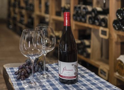 Eine Flasche St. Magdalener Wein steht mit zwei Weingläsern und Trauben auf einem Tisch im Weinkeller.
