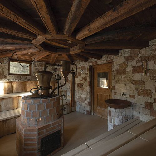 Ein rustikaler Saunaraum mit Holzbänken, Steinwänden und einem Ofen unter einer dunklen Holzdecke.