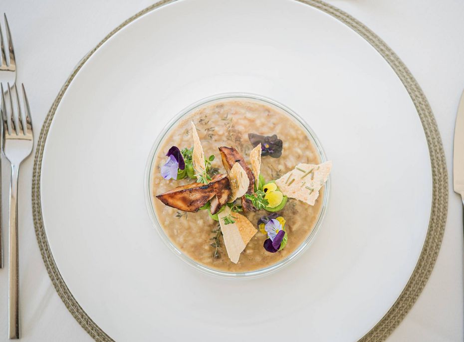 Gourmetgericht im Preidlhof in Naturns Eine feine Vorspeise in einer Schale liegt auf einem gedeckten Tisch mit Besteck und weißem Teller.