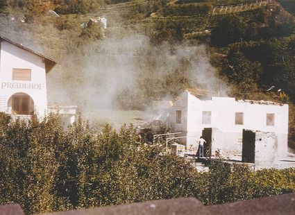 Eine historische Aufnahme zeigt Gebäude des Preidlhofs in Naturns mit aufsteigendem Dampf vor dem Hang.