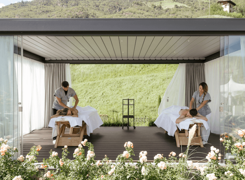 Paarmassage im Outdoor-Spa im Preidlhof Zwei Therapeutinnen behandeln zwei Gäste auf Liegen in einem offenen Spa-Pavillon mit Blick ins Grüne.