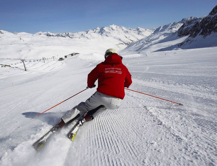 Ein Skifahrer fährt auf einer präparierten Piste inmitten verschneiter Berge.