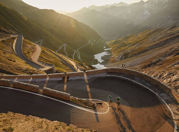 Due ciclisti percorrono una strada di montagna tortuosa sopra una valle al tramonto.