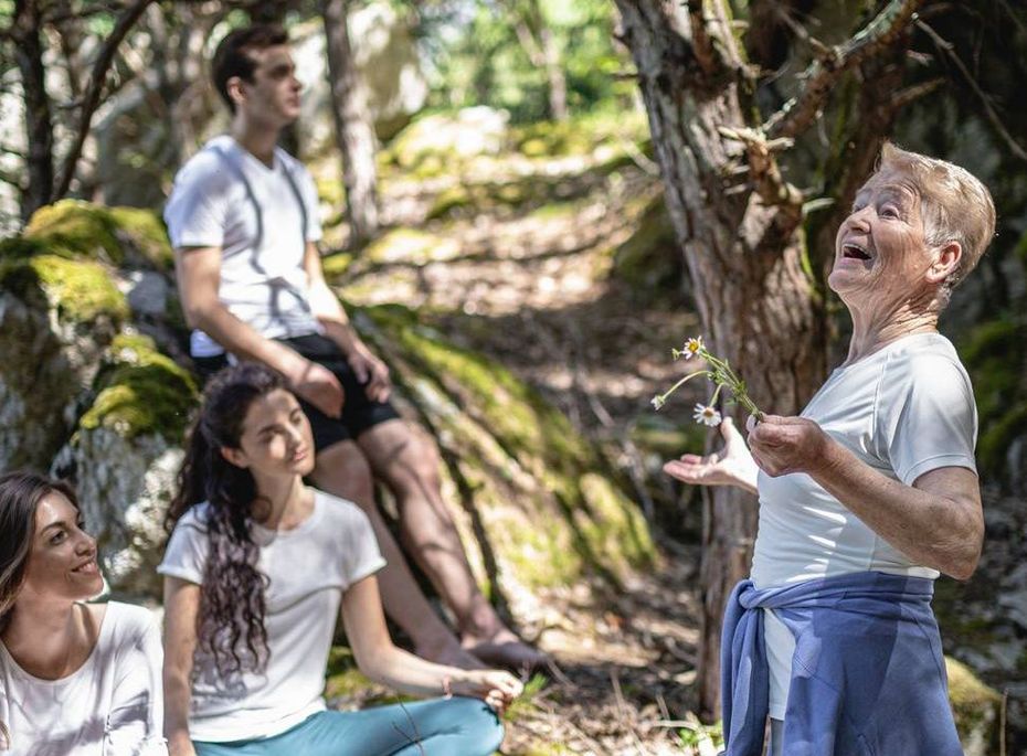 Drei sitzende Personen hören einem Mann beim Wandern im Wald zu.