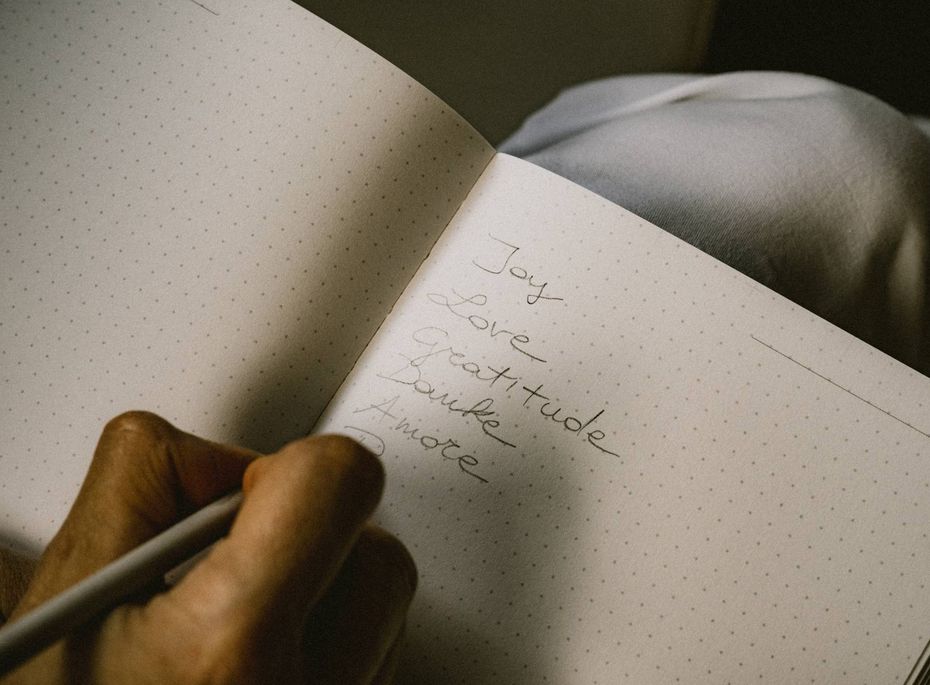 Eine Hand schreibt mit einem Stift handschriftliche Gedanken in ein aufgeschlagenes Notizbuch.