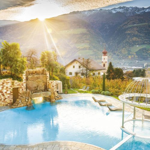 Ein Infinity-Pool mit Liegen, Palmengarten und Bergpanorama im Sonnenlicht.