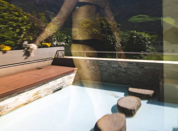 A small outdoor pool terrace beside a glass-walled sauna area with stone stepping seats.