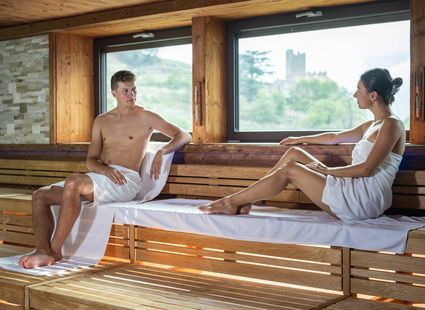 Ein Mann und eine Frau sitzen in einer Sauna auf einer Holzbank und blicken sich an.