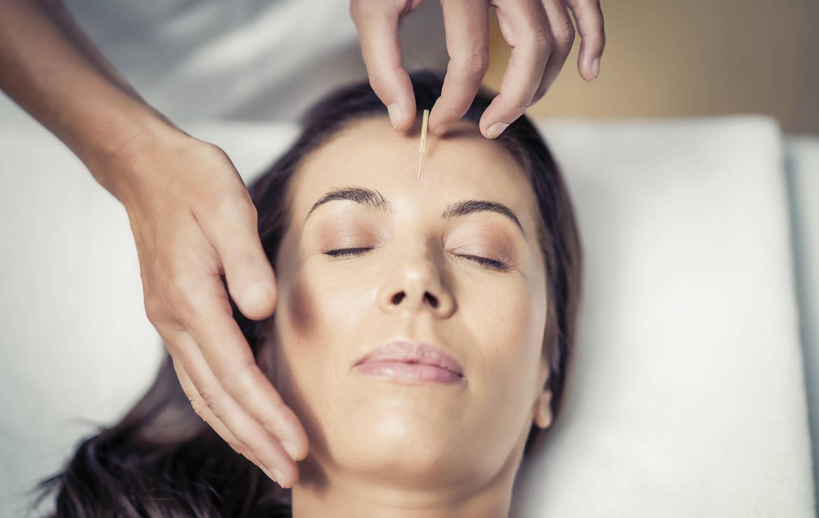 Una donna riceve un trattamento viso mentre un operatore lavora sulla fronte e sul viso.