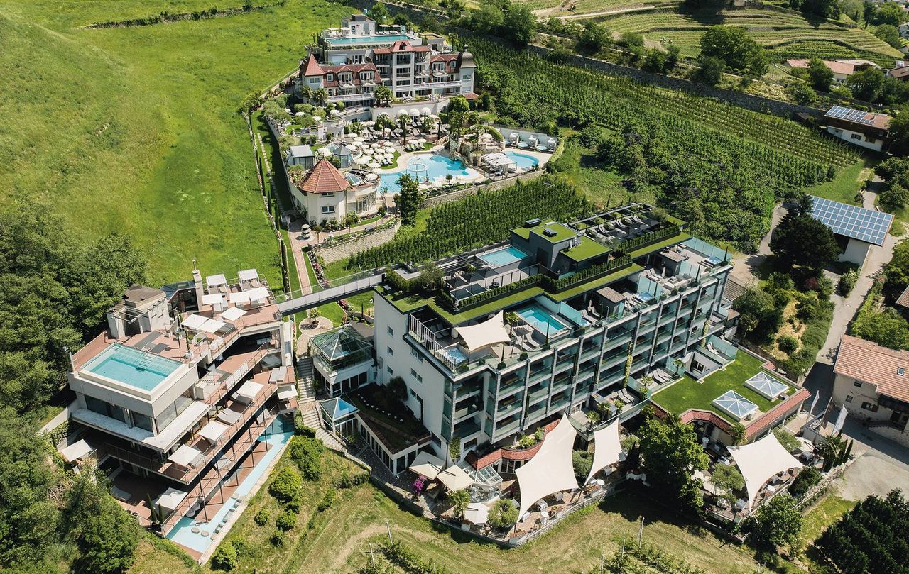 Luftaufnahme des Wellnesshotels Preidlhof mit Poolanlage, Terrassen und Garten inmitten von Weinbergen.