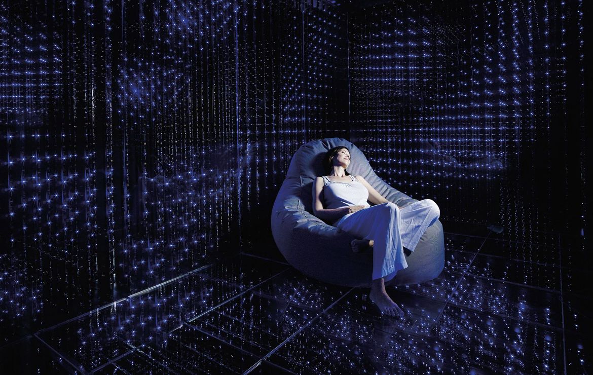 Una donna si rilassa su una poltrona reclinabile in una stanza spa buia con giochi di luce blu.