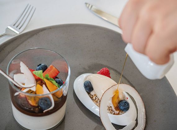 A plated gourmet dessert with berries and cream is being finished with a drizzle of sauce.
