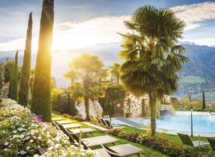 Ein Infinity Pool liegt in einer gepflegten Gartenanlage mit Liegen, Palmen und Bergblick im warmen Abendlicht.