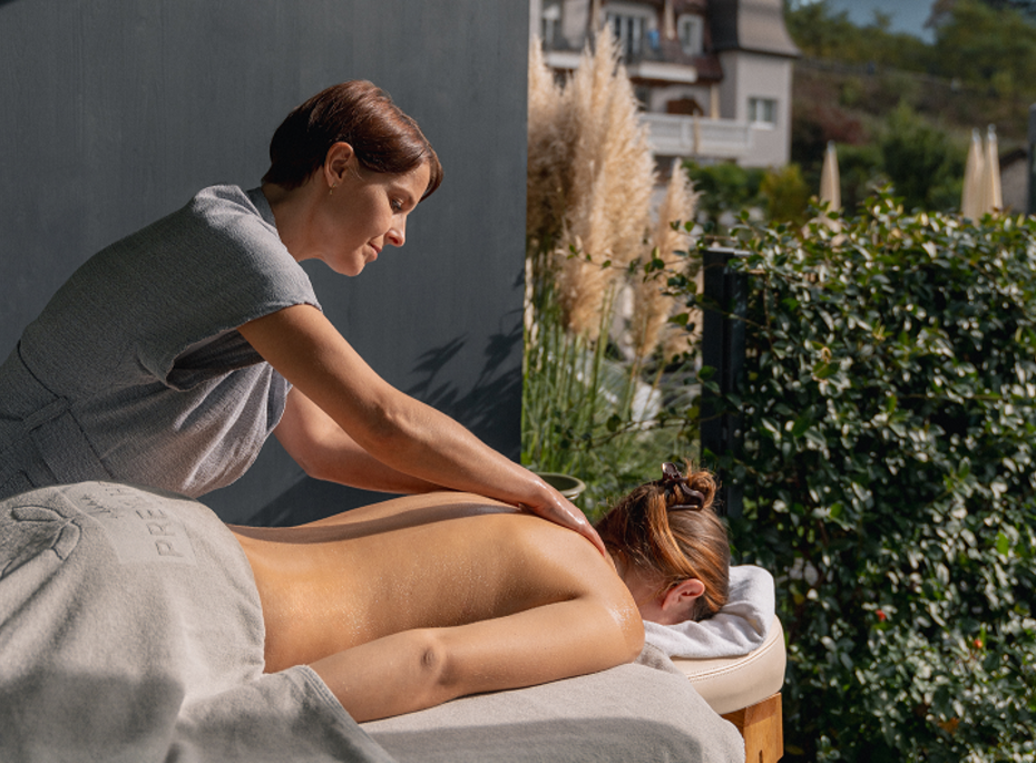 Massage im Freien im Preidlhof Eine Therapeutin massiert auf einer Liege im Freien den Rücken einer entspannten Frau.