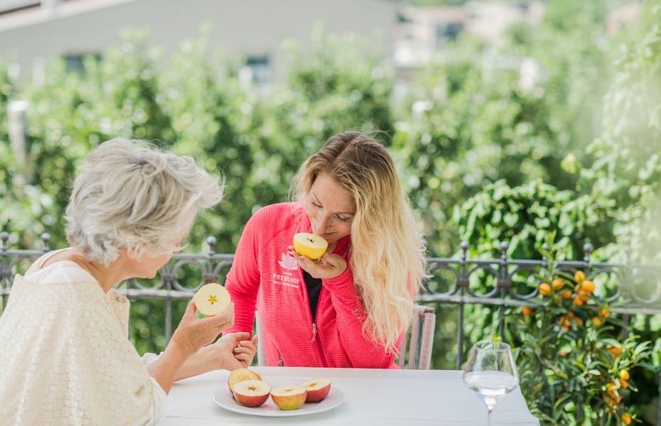 Wellness-Snack auf der Terrasse im Preidlhof Zwei Frauen sitzen draußen an einem Tisch und essen einen Obstsnack auf der Terrasse.