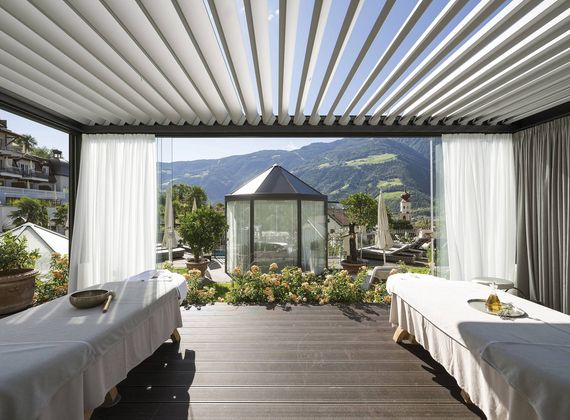 Una terrazza wellness coperta con due lettini, un padiglione in vetro e vista sulle montagne.