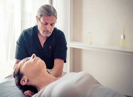 Ein Therapeut behandelt eine liegende Frau mit einer Massage in einem hellen Spa-Raum.