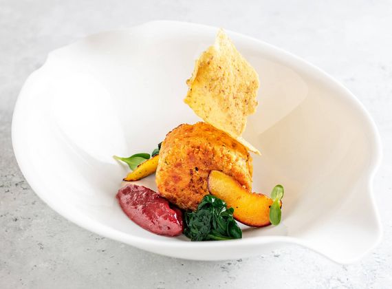 A gourmet dish is plated in a white bowl with beetroot, vegetables, a crisp garnish and a creamy sauce.