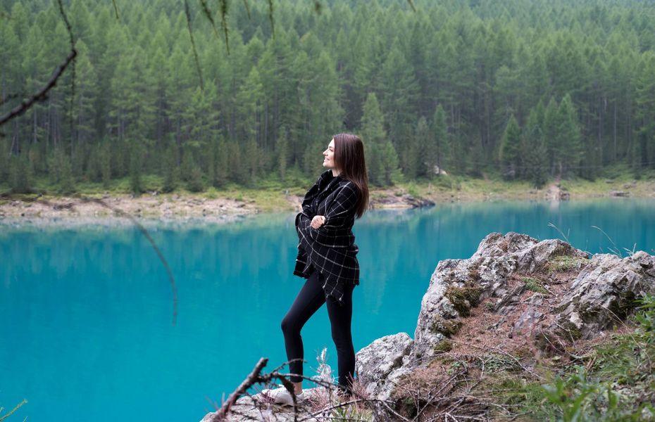 Frau am Seeufer im Natururlaub Eine Frau steht auf einem Felsen am türkisblauen Seeufer vor dichtem Nadelwald.
