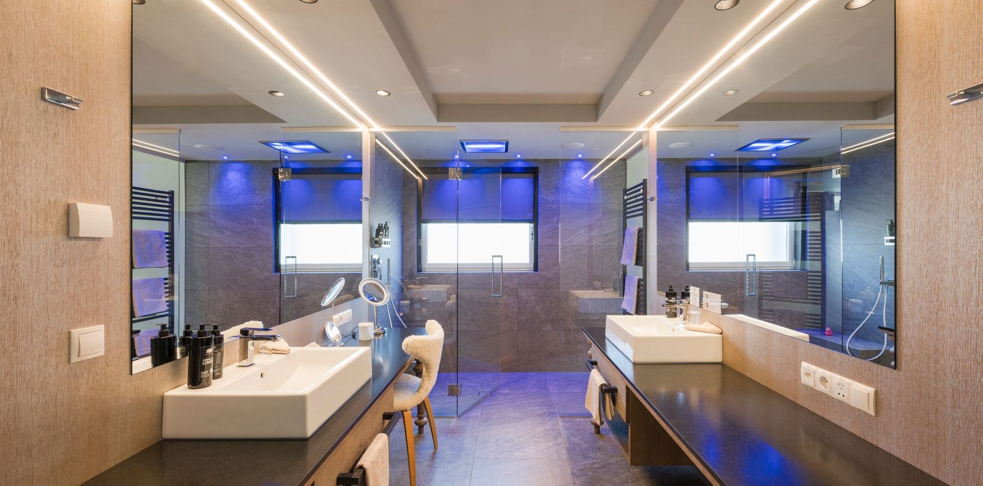 Ein modernes Suite-Bad mit zwei Waschbecken, großen Spiegeln und blauer Akzentbeleuchtung.
