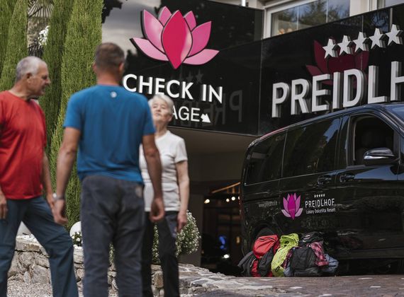 Drei Gäste stehen vor dem Check-in des Preidlhof in Naturns, daneben ein schwarzes Fahrzeug mit Gepäck.